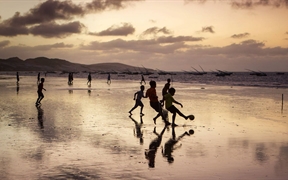  巴西福塔雷萨 ，一群男孩儿在日落时分的沙滩上踢足球